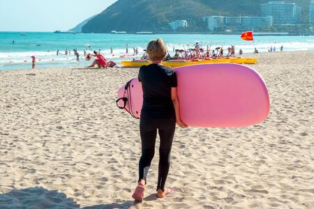 Surfing. Young girl with a surfboard goes on the beach. Extreme water sports. Healthy active lifestyle. Summer vacationの写真素材