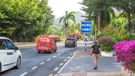 Sanya, Hainan, China - May 16, 2019: a young girl traveler with a backpack is walking along the road, rear view. Along the edges of the road is dense tropical exotic vegetation. Intensive traffic.のeditorial素材