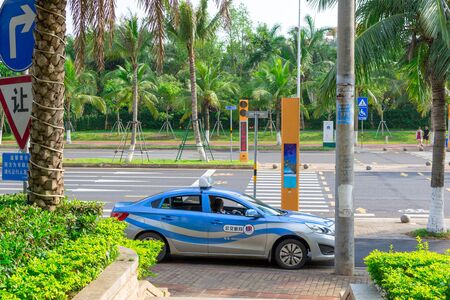 Haikou, Hainan, China - May 12, 2019: Blue taxi car waiting passenger. Along the edges of the street dense tropical vegetation, palm trees.のeditorial素材