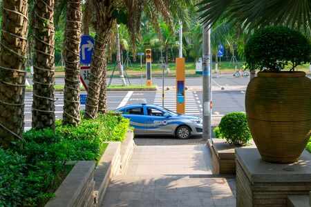 Haikou, Hainan, China - May 12, 2019: Blue taxi car waiting passenger. Along the edges of the street dense tropical vegetation, palm trees.のeditorial素材