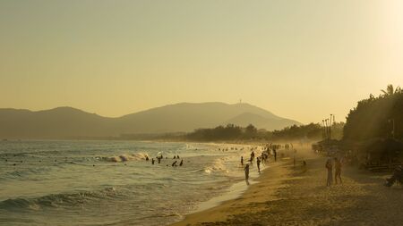 Tropical beach, people having fun in the sea, the golden twilight of sunset light. Soft focusの写真素材