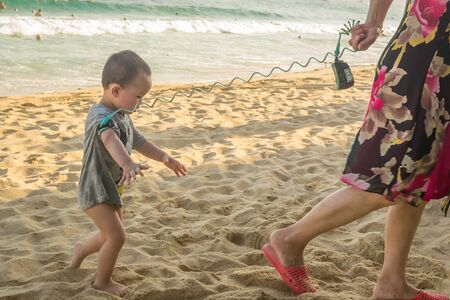 Hainan, China - May 15, 2019: a woman leads a small child tied on a leash on the beachのeditorial素材