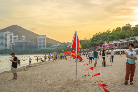Hainan, China - May 14, 2019: Tropical beach, people swim in the sea, rest on the sand, golden twilight of sunset lightのeditorial素材