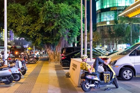 Sanya, Hainan, China - May 17, 2019: In nighttime the courier of the parcel delivery service is resting. The Meituan Delivery service offers a short distance delivery service.のeditorial素材