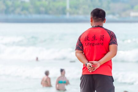 A Chinese lifeguard on Sanya beach keeps order and safety. In the hands of a whistle to ensure the discipline of tourists on the water. T-shirt with the inscription Lifeguard in English and Chinese.の写真素材