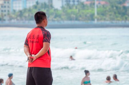 A Chinese lifeguard on Sanya beach keeps order and safety. In the hands of a whistle to ensure the discipline of tourists on the water. T-shirt with the inscription Lifeguard in English and Chinese.の写真素材