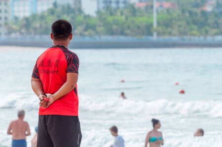 A Chinese lifeguard on Sanya beach keeps order and safety. In the hands of a whistle to ensure the discipline of tourists on the water. T-shirt with the inscription Lifeguard in English and Chinese.の写真素材