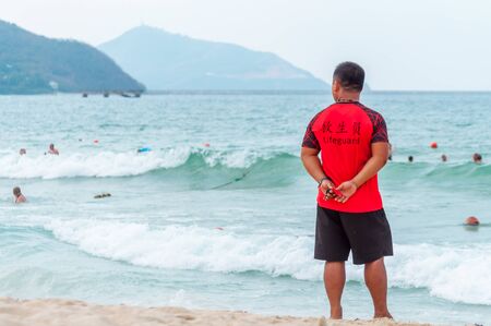 A Chinese lifeguard on Sanya beach keeps order and safety. In the hands of a whistle to ensure the discipline of tourists on the water. T-shirt with the inscription Lifeguard in English and Chinese.の写真素材