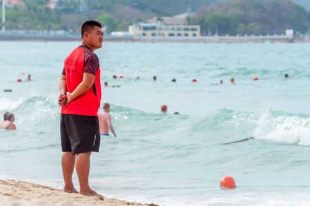 Sanya, China - May 15, 2019: A lifeguard on beach keeps order and safety. In the hands of a whistle to ensure the discipline. T-shirt with the inscription Lifeguard in English and Chinese.のeditorial素材