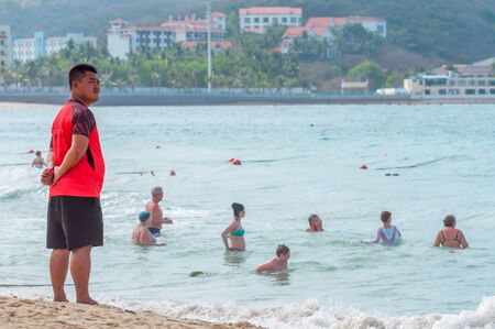Sanya, China - May 15, 2019: A lifeguard on beach keeps order and safety. In the hands of a whistle to ensure the discipline. T-shirt with the inscription Lifeguard in English and Chinese.のeditorial素材