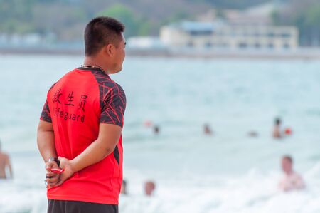 Sanya, China - May 15, 2019: A lifeguard on beach keeps order and safety. In the hands of a whistle to ensure the discipline. T-shirt with the inscription Lifeguard in English and Chinese.のeditorial素材