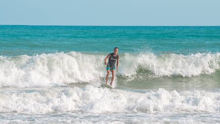 Sanya, hainan, China - May 16, 2019: An unknown young muscular surfer slides beautifully through the azure waves of the South China Sea on a surfboard. Surfing is an extreme beautiful sport.のeditorial素材