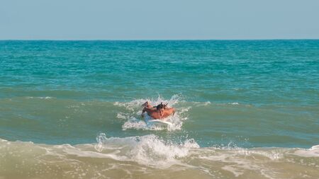 Sanya, hainan, China - May 16, 2019: An unknown young muscular surfer actively rows his hands on a surfboard to catch a big wave of the South China Sea. Surfing is a beautiful and extreme sport.のeditorial素材