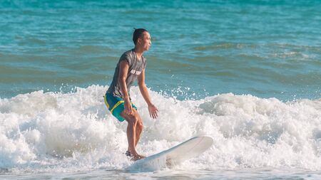 Sanya, hainan, China - May 16, 2019: An unknown young muscular surfer slides beautifully through the azure waves of the South China Sea on a surfboard. Surfing is an extreme beautiful sport.のeditorial素材