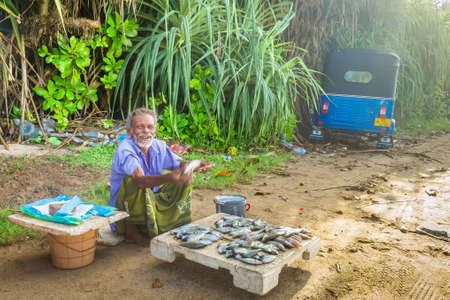 Koggala, Sri Lanka - May, 2016: A street seller of fresh fish offers to buy goods from him. Nearby stands his vehicle - tuk-tuk.のeditorial素材