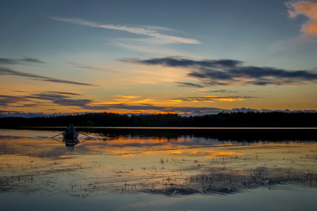 Two people are sailing in a boat. Beautiful sunset landscape over a Finnish lake. The space is flooded with goldの写真素材