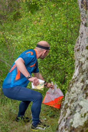 Village of Aktovo, Ukraine - May 21, 2021: Orienteering race. Traditional annual orienteering game Partisan Spark Cup 2021. Athlete marks the passage of the control pointのeditorial素材