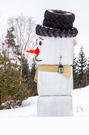 Snowman made from agricultural hay rolls packed in white plastic. There are car tires on the snowman's headの写真素材