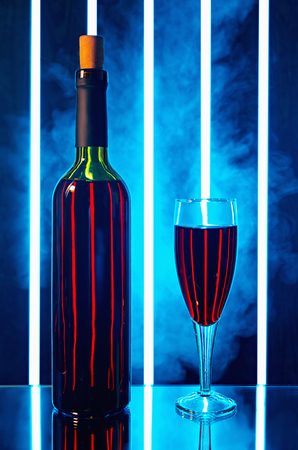 bottle of red wine in the smoke in the background is a bright vertical light strip and stand on the table mirroredの写真素材