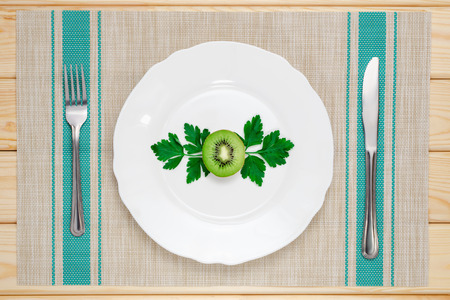 kiwi and parsley on a white plate with knife and fork on the tableclothの写真素材