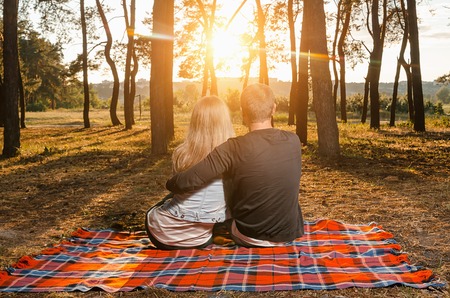 Loving couple sitting embracing on the bedspread during sunsetの写真素材