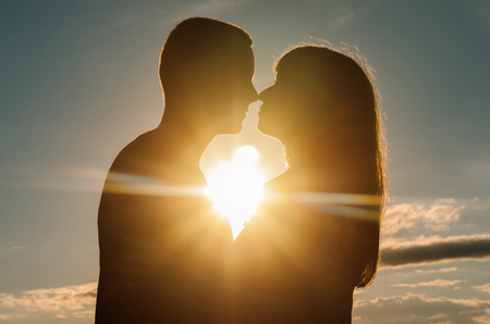 silhouette of loving couple embracing at sunset, the rays of the sunの写真素材