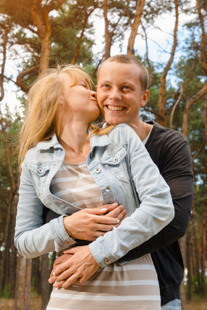 young couple stand embracing in the woods, kiss on the cheekの写真素材