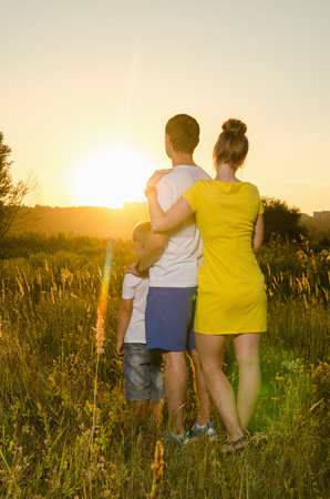 happy family standing outdoors on the field embracing watching the sunsetの写真素材