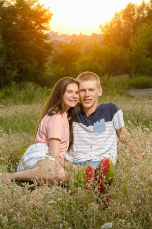 happy loving couple sitting on a field on a background magic sunsetの写真素材