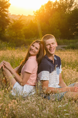 happy loving couple sitting on a field on a background magic sunsetの写真素材