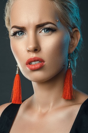 frowning blonde, trendy studio portrait with red earringsの写真素材
