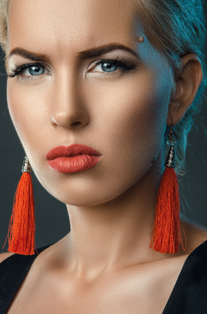 frowning blonde, trendy studio portrait with red earringsの写真素材