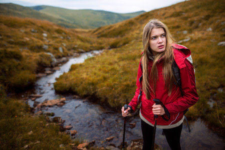 Shot of a young woman looking at the landscape while hiking in the mountains.Outdoor shot of attractive young woman with backpack standing in a mountain stream. Female hiker in creek water.の写真素材