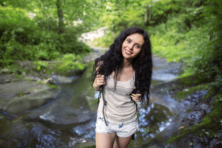 Portrait of beautiful young woman with backpack standing by the creek. Female hiker hiking by the mountain stream.の写真素材
