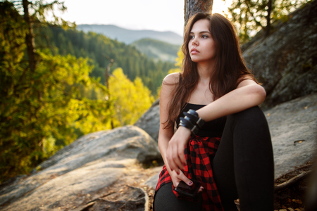 Young tourist relaxing on rock and enjoying sunset. Backpacker a young woman sitting on rock in mountainsの写真素材