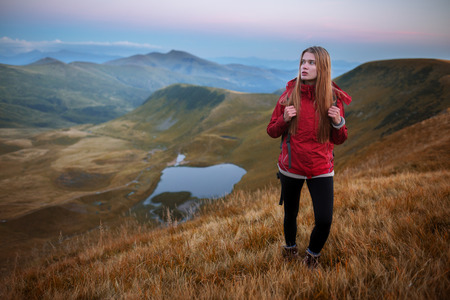 Female hiker with backpack standing on top of mountain. Shot of a young woman looking at the landscape while hiking in the mountainsの写真素材