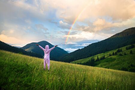 Positive young woman hiker in pink Dragon Pajamas open arms at mountain peak. Slim lady in pink night-suit. Funny travel, Animal Cosplay Costume. Summer adventure journey in mountain nature outdoorsの写真素材