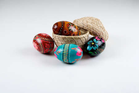 One wooden easter egg in a basket and three painted wooden easter eggs beside on a white background.