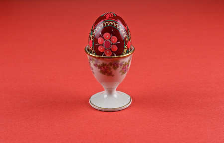 A wooden red easter egg in a white holder isolate on a red background.の写真素材
