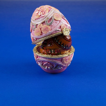 A wooden easter egg inside in a ceramic handmade easter egg isolated on a blue background.の写真素材