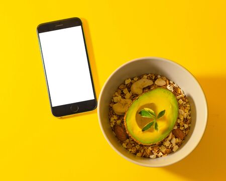 homemade Granola baked with avocado and phone on yellow background. Healthy breakfast.の写真素材