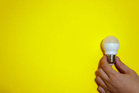 Caucasian's hand hold white eco lamp bulb isolated on yellow background. Business concept. Copy...