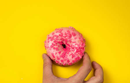 Hand hold pink donut with sprinkles on yellow background.の写真素材