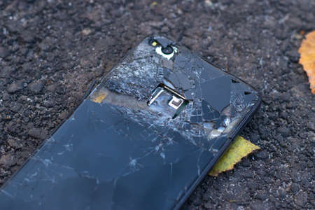 Smart phone with broken screen glass on the ground. Broken black phone. Close up.の写真素材