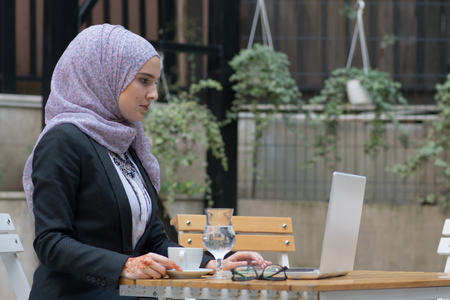 Young muslim girl typing on laptop and drink coffeeの写真素材