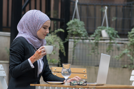 Young muslim girl typing on laptop and drink coffeeの写真素材