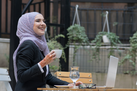 Young muslim girl typing on laptop and drink coffeeの写真素材