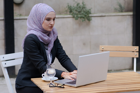 Young muslim girl typing on laptop and drink coffeeの写真素材