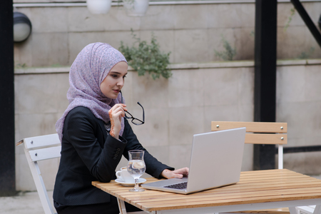 Young muslim girl typing on laptop and drink coffeeの写真素材