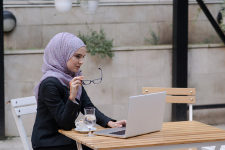 Young muslim girl typing on laptop and drink coffeeの写真素材